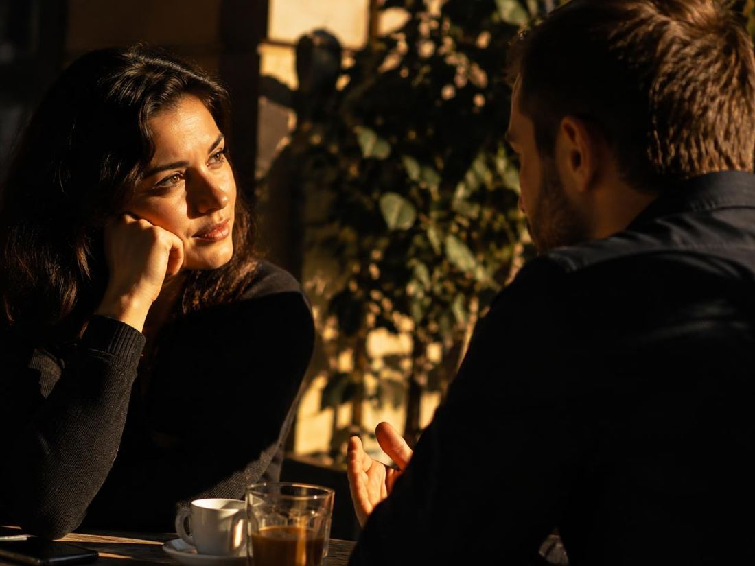 Duas pessoas conversando atentamente à mesa de um café sob luz quente